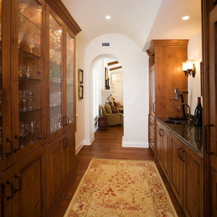 Diseño de bar en casa con fregadero de galera, mediterráneo, de tamaño medio, con fregadero bajoencimera, armarios con paneles con relieve, puertas de armario de madera oscura, encimera de granito, suelo de madera en tonos medios y suelo marrón