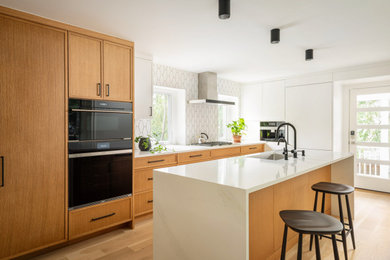 Trendy galley light wood floor and beige floor kitchen photo in Philadelphia with an undermount sink, shaker cabinets, medium tone wood cabinets, white backsplash, mosaic tile backsplash, black appliances, an island and white countertops