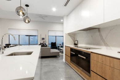 Design ideas for a mid-sized contemporary galley open plan kitchen in Perth with an undermount sink, flat-panel cabinets, medium wood cabinets, solid surface benchtops, white splashback, ceramic splashback, black appliances, ceramic floors, with island, grey floor and white benchtop.