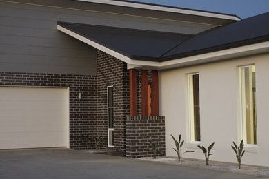 Mid-sized contemporary one-storey brick grey exterior in Other with a hip roof.