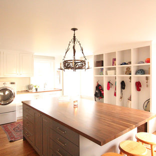 他の地域の大きいトランジショナルスタイルのおしゃれな家事室 (ドロップインシンク、レイズドパネル扉のキャビネット、白いキャビネット、木材カウンター、グレーの壁、無垢フローリング、左右配置の洗濯機・乾燥機、茶色い床) の写真