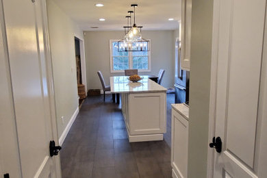 Eat-in kitchen - mid-sized transitional l-shaped porcelain tile and gray floor eat-in kitchen idea in New York with a farmhouse sink, shaker cabinets, white cabinets, quartz countertops, white backsplash, subway tile backsplash, stainless steel appliances, an island and white countertops