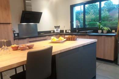 Idées déco pour une très grande cuisine noire et bois contemporaine en bois clair fermée avec un évier 2 bacs, un placard à porte plane, un plan de travail en stratifié, une crédence noire, un électroménager noir, un sol en carrelage de céramique, îlot, un sol noir et plan de travail noir.