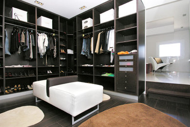 Ejemplo de vestidor unisex actual de tamaño medio con armarios abiertos, puertas de armario negras, suelo marrón y suelo de madera oscura