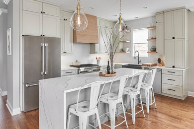Mid-sized transitional u-shaped medium tone wood floor eat-in kitchen photo in Chicago with a farmhouse sink, recessed-panel cabinets, white cabinets, quartzite countertops, white backsplash, porcelain backsplash, black appliances, an island and white countertops