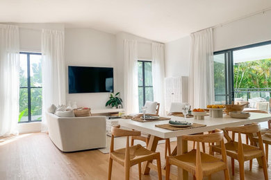 Imagen de sala de estar abierta minimalista grande con paredes blancas, suelo de madera en tonos medios y televisor colgado en la pared