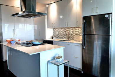 Mid-sized minimalist l-shaped dark wood floor and brown floor open concept kitchen photo with an undermount sink, flat-panel cabinets, white cabinets, quartz countertops, mosaic tile backsplash, stainless steel appliances, an island, beige countertops and multicolored backsplash