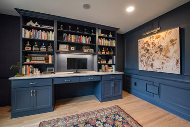 Modelo de despacho minimalista de tamaño medio con paredes azules, suelo de madera clara, escritorio empotrado y boiserie