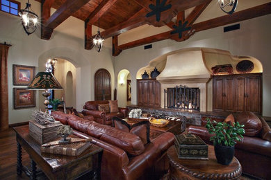 Huge tuscan open concept dark wood floor and brown floor living room photo in Phoenix with beige walls, a standard fireplace, a plaster fireplace and a concealed tv