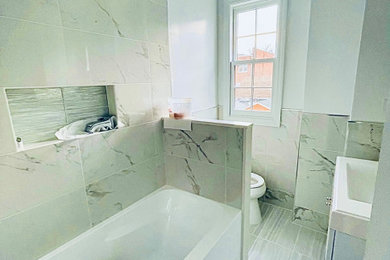 Example of a small trendy master multicolored tile and ceramic tile ceramic tile, gray floor and single-sink alcove bathtub design with glass-front cabinets, white cabinets, a one-piece toilet, gray walls, marble countertops, a hinged shower door, gray countertops, a niche and a floating vanity