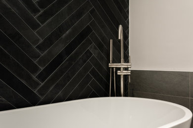Diseño de cuarto de baño principal, blanco y gris y negro ecléctico de tamaño medio con bañera exenta, baldosas y/o azulejos negros, baldosas y/o azulejos de pizarra, paredes grises, suelo de baldosas de porcelana y suelo gris