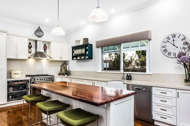 Large country l-shaped eat-in kitchen in Melbourne with a farmhouse sink, recessed-panel cabinets, white cabinets, wood benchtops, beige splashback, stone slab splashback, stainless steel appliances, dark hardwood floors and with island.