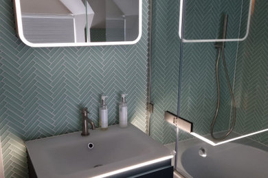 Photo of a medium sized contemporary family bathroom in Gloucestershire with freestanding cabinets, green cabinets, a built-in bath, a built-in shower, a wall mounted toilet, blue tiles, ceramic tiles, a wall-mounted sink, glass worktops, a hinged door, white worktops, a single sink and a floating vanity unit.