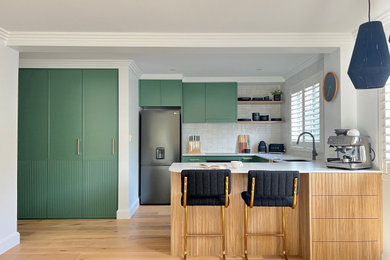 Mid-sized contemporary u-shaped open plan kitchen in Sydney with an undermount sink, recessed-panel cabinets, green cabinets, quartz benchtops, yellow splashback, porcelain splashback, black appliances, medium hardwood floors, a peninsula, brown floor and white benchtop.