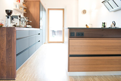 Offene, Zweizeilige, Geräumige Moderne Küche mit Einbauwaschbecken, flächenbündigen Schrankfronten, dunklen Holzschränken, Arbeitsplatte aus Holz, Küchenrückwand in Weiß, schwarzen Elektrogeräten, hellem Holzboden, Kücheninsel, braunem Boden und brauner Arbeitsplatte in Dortmund