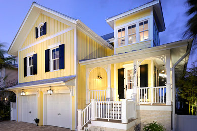 Design ideas for a large beach style two-storey yellow house exterior in Tampa with wood siding, a flat roof and a shingle roof.