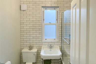 Inspiration for a small victorian cream and black bathroom in London with an alcove bath, a shower/bath combination, a two-piece toilet, beige tiles, ceramic tiles, beige walls, ceramic flooring, a pedestal sink, black floors, a hinged door, a wall niche and a single sink.