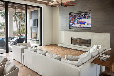Large beach style enclosed light wood floor and brown floor family room photo in Other with a wall-mounted tv, white walls, a ribbon fireplace and a concrete fireplace
