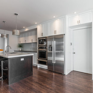 Large contemporary kitchen pantry inspiration - Example of a large trendy galley dark wood floor kitchen pantry design in Montreal with an undermount sink, shaker cabinets, white cabinets, marble countertops, white backsplash, glass sheet backsplash, stainless steel appliances and an island