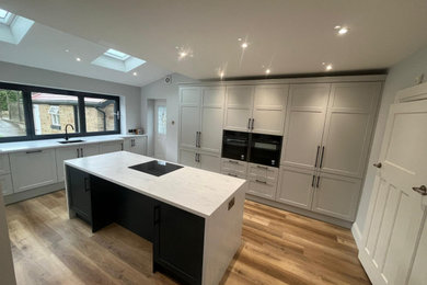 Photo of a large classic open plan kitchen in Other with a single-bowl sink, shaker cabinets, grey cabinets, composite countertops, white splashback, black appliances, laminate floors, an island, brown floors and white worktops.
