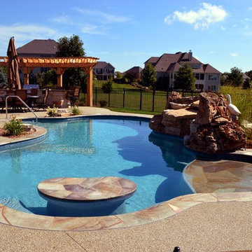Free form pool with stone table, sun shelf, water feature, and outdoor kitchen,