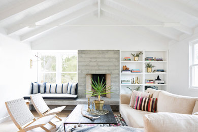 This is an example of a beach style living room in San Diego with a concrete fireplace surround, white walls, a standard fireplace and no tv.