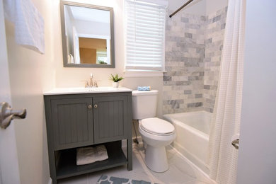 Photo of a small transitional 3/4 bathroom in Atlanta with furniture-like cabinets, grey cabinets, an alcove tub, a shower/bathtub combo, a two-piece toilet, multi-coloured tile, subway tile, white walls, ceramic floors, an integrated sink, engineered quartz benchtops, grey floor and a shower curtain.