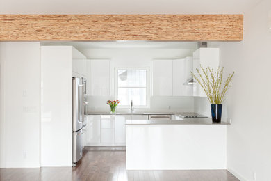 This is an example of a mid-sized modern u-shaped open plan kitchen in Vancouver with flat-panel cabinets, white cabinets, stainless steel appliances, medium hardwood floors, a peninsula and brown floor.