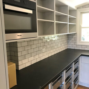 Small contemporary kitchen pantry designs - Small trendy galley medium tone wood floor kitchen pantry photo in Wollongong with white cabinets, white backsplash, subway tile backsplash, stainless steel appliances and no island