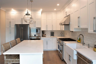 This is an example of a contemporary l-shaped kitchen in Vancouver with an undermount sink, recessed-panel cabinets, white cabinets, quartzite benchtops, white splashback, subway tile splashback, stainless steel appliances, laminate floors, with island, brown floor and white benchtop.