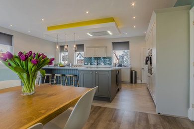 Inspiration for a large contemporary open plan kitchen in Cheshire with a drop-in sink, recessed-panel cabinets, white cabinets, quartz benchtops, blue splashback, subway tile splashback, panelled appliances, light hardwood floors and with island.