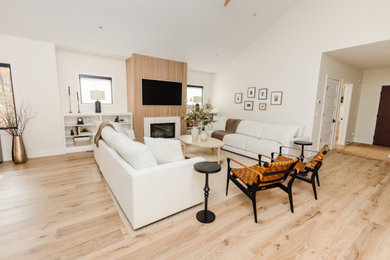 Inspiration for a mid-sized scandinavian medium tone wood floor, beige floor and vaulted ceiling living room remodel in Other with white walls, a standard fireplace, a wood fireplace surround and a wall-mounted tv