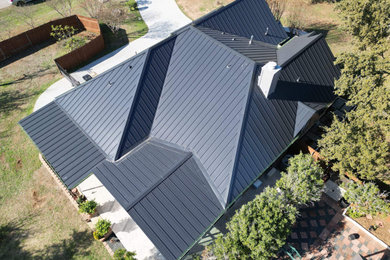 Large minimalist one-story house exterior photo in Austin with a hip roof, a metal roof and a black roof