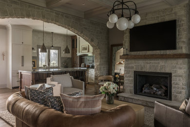 Mid-sized french country medium tone wood floor, brown floor and coffered ceiling living room photo in Other with a standard fireplace, a stone fireplace, a wall-mounted tv and gray walls