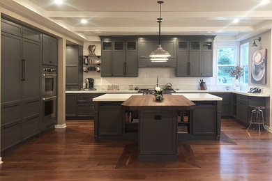 Large transitional open plan kitchen in Los Angeles with recessed-panel cabinets, grey cabinets, white splashback, porcelain splashback, medium hardwood floors, with island, a farmhouse sink, panelled appliances and brown floor.