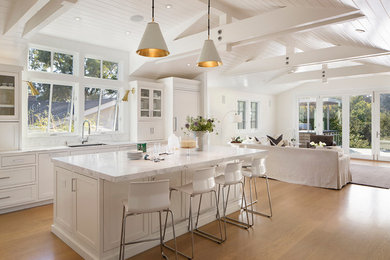 Beach style light wood floor open concept kitchen photo in San Francisco with a single-bowl sink, recessed-panel cabinets, white cabinets, marble countertops, white backsplash, stone tile backsplash, stainless steel appliances and an island