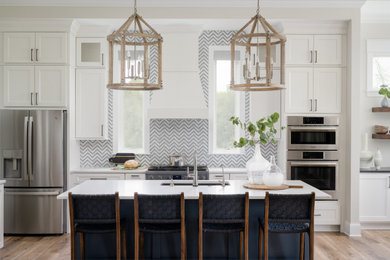 Example of a mid-sized trendy l-shaped medium tone wood floor eat-in kitchen design in Indianapolis with an undermount sink, shaker cabinets, white cabinets, quartz countertops, stainless steel appliances, an island and white countertops