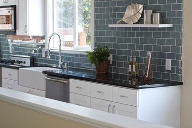 Eat-in kitchen - large contemporary l-shaped medium tone wood floor eat-in kitchen idea in San Francisco with a farmhouse sink, shaker cabinets, white cabinets, solid surface countertops, green backsplash, subway tile backsplash, stainless steel appliances and no island
