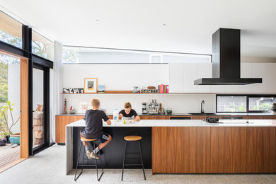 Large contemporary galley open plan kitchen in Sydney with a double-bowl sink, flat-panel cabinets, medium wood cabinets, marble benchtops, white splashback, brick splashback, black appliances, concrete floors, with island, grey floor and black benchtop.
