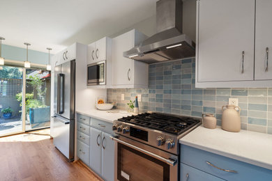 Example of a mid-sized 1950s u-shaped medium tone wood floor and brown floor eat-in kitchen design in Portland with shaker cabinets, blue cabinets, quartz countertops, blue backsplash, porcelain backsplash, stainless steel appliances, no island and white countertops
