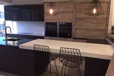 Mid-sized modern u-shaped eat-in kitchen in Brisbane with an undermount sink, glass-front cabinets, brown cabinets, granite benchtops, white splashback, stone slab splashback, black appliances and multiple islands.