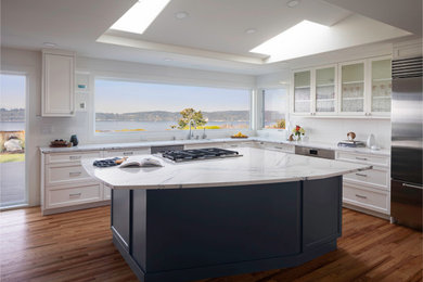 Large minimalist light wood floor, brown floor and vaulted ceiling eat-in kitchen photo in Seattle with a double-bowl sink, recessed-panel cabinets, white cabinets, granite countertops, white backsplash, ceramic backsplash, stainless steel appliances, an island and white countertops