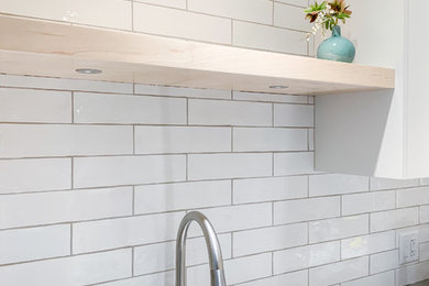Inspiration for a mid-sized scandinavian l-shaped medium tone wood floor eat-in kitchen remodel in Vancouver with a single-bowl sink, flat-panel cabinets, white cabinets, quartz countertops, white backsplash, ceramic backsplash, stainless steel appliances, a peninsula and gray countertops