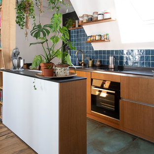 Неиссякаемый источник вдохновения для домашнего уюта: маленькая параллельная кухня-гостиная в стиле фьюжн с плоскими фасадами, синим фартуком, фартуком из керамической плитки, черной техникой, полом из керамической плитки, синим полом, черной столешницей, фасадами цвета дерева среднего тона, полуостровом, врезной раковиной и столешницей из акрилового камня