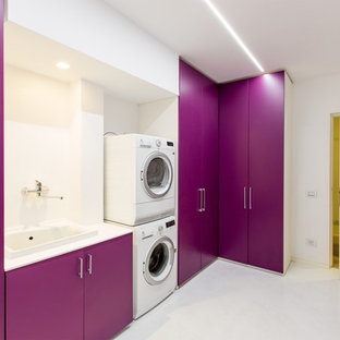 Contemporary single-wall separated utility room in Other with a built-in sink, flat-panel cabinets, white walls and a stacked washer and dryer.