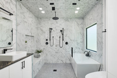 Medium sized modern ensuite wet room bathroom in Other with flat-panel cabinets, white cabinets, a freestanding bath, a wall mounted toilet, white tiles, porcelain tiles, white walls, porcelain flooring, a vessel sink, quartz worktops, grey floors, an open shower, black worktops, a wall niche, double sinks and a built in vanity unit.
