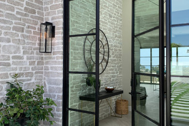 Mid-sized beach style porcelain tile, beige floor and brick wall entryway photo in Orange County with beige walls and a black front door