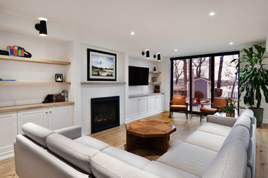 This is an example of a large beach style open concept living room in Toronto with white walls, light hardwood floors, a standard fireplace, a wall-mounted tv and brown floor.