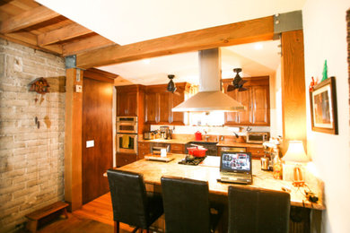 Inspiration for a rustic single-wall medium tone wood floor and brown floor open concept kitchen remodel in Los Angeles with an undermount sink, raised-panel cabinets, medium tone wood cabinets, granite countertops, multicolored backsplash, stone slab backsplash, stainless steel appliances, an island and multicolored countertops