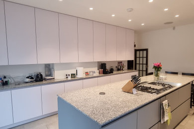Inspiration for an expansive modern grey and white galley kitchen/diner in London with an integrated sink, flat-panel cabinets, white cabinets, granite worktops, white splashback, stainless steel appliances, terracotta flooring, an island, beige floors, grey worktops and feature lighting.